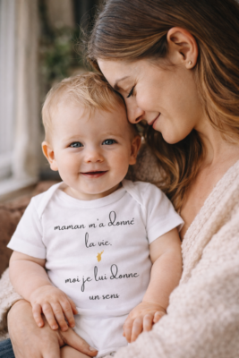 Bébé portant un body avec le message « Maman m’a donné la vie, moi je lui donne un sens », blotti contre sa maman